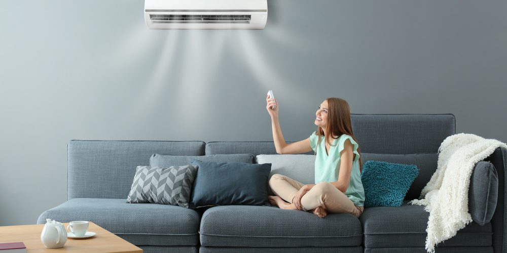 Young,Woman,Switching,On,Air,Conditioner,While,Sitting,On,Sofa How to Decide Whether to Repair or Replace an Air Conditioner