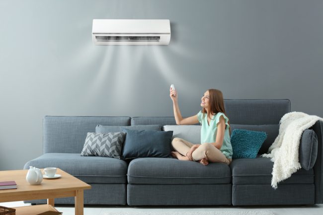 Young,Woman,Switching,On,Air,Conditioner,While,Sitting,On,Sofa How to Decide Whether to Repair or Replace an Air Conditioner