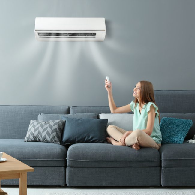 Young,Woman,Switching,On,Air,Conditioner,While,Sitting,On,Sofa How to Decide Whether to Repair or Replace an Air Conditioner
