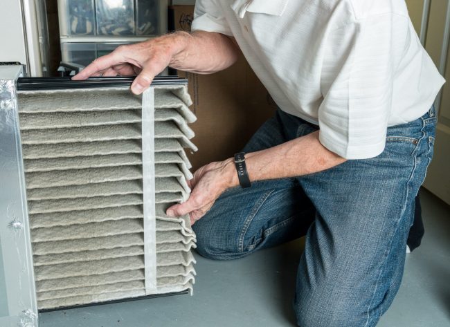Furnace Maintenance man changing a folded dirty air filter in the HVAC furnace system