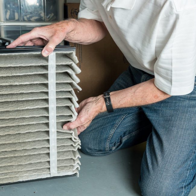 Furnace Maintenance man changing a folded dirty air filter in the HVAC furnace system