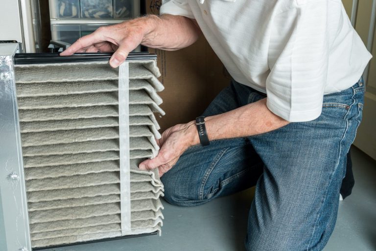 Furnace Maintenance man changing a folded dirty air filter in the HVAC furnace system