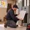 An HVAC technician kneels, holding a clean furnace filter, preparing to install it into a grey furnace unit, a key step in fall furnace maintenance.
